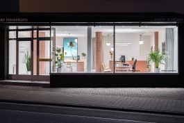 Reisebüro Einhausen Innenarchitektur Design - Blick durch Schaufenster bei Abend in den hell beleuchteten Innenraum mit Display und Pflanzen 